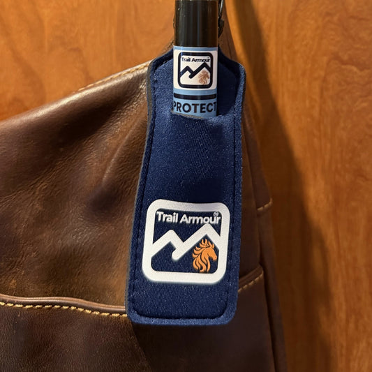 Trail Armour PROTECT lip balm sitting in a navy neoprene Trail Armour holder clipped to a bag