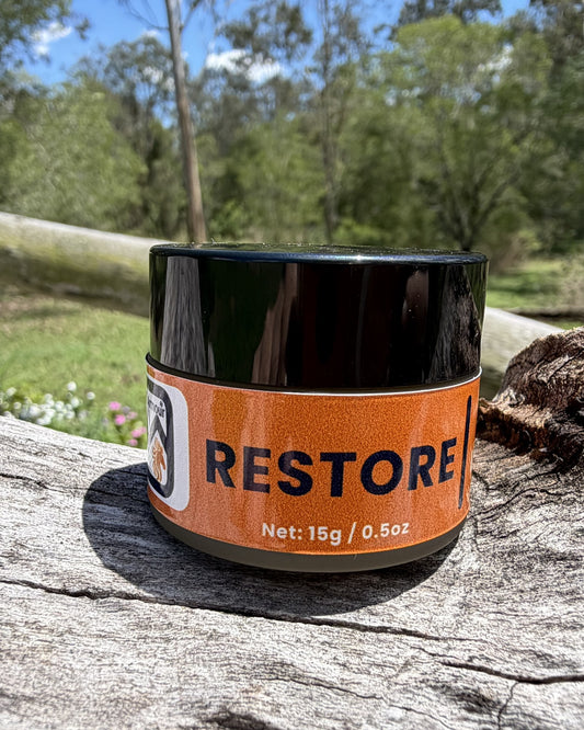 Trail Armour RESTORE overnight lip treatment jar on a weathered log with bushland and blue sky behind